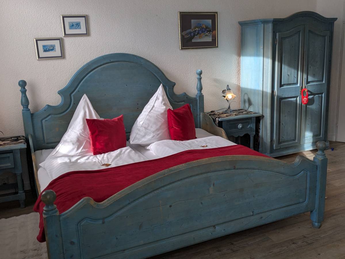 Komfortables Doppelzimmer im Hotel Jägerhof in Mayen mit einem Doppelbett, dekoriert mit roten Kissen und einer gemütlichen Kuscheldecke. Das Zimmer verfügt über ein eigenes Bad mit Dusche und Kosmetikspiegel und wird täglich für Sie gereinigt.